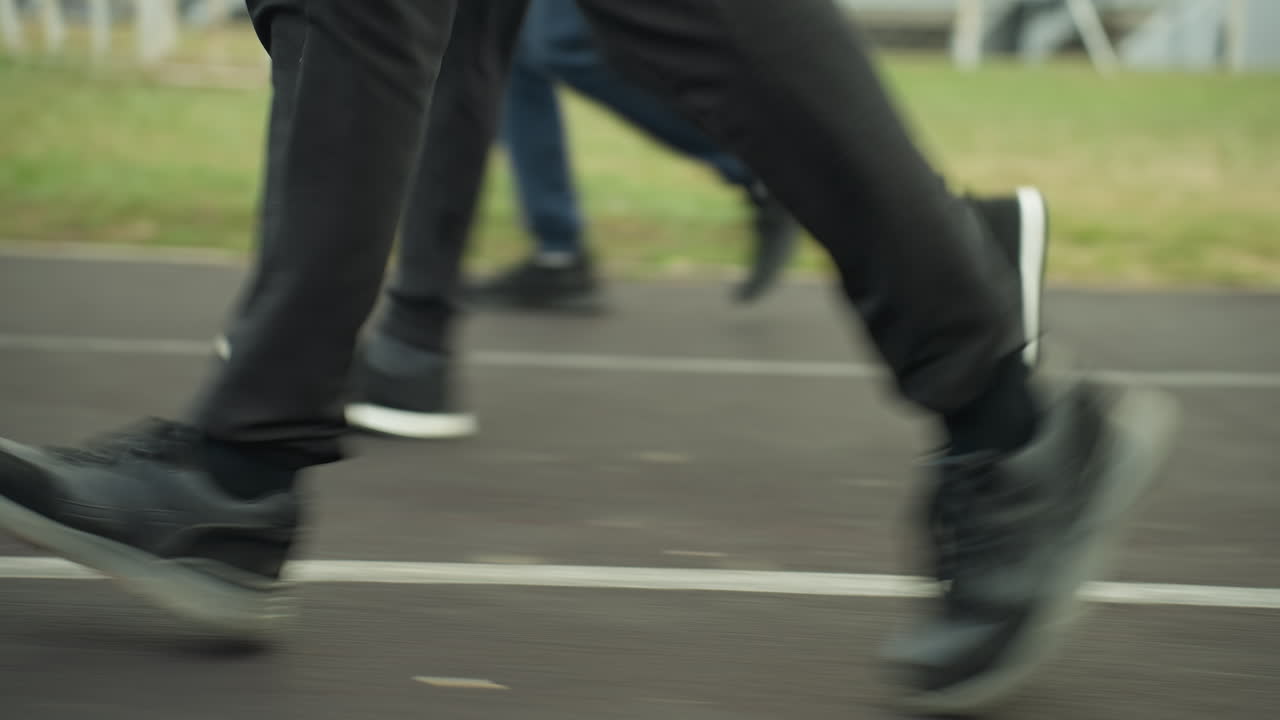 Close-up leg view of three people wearing joggers and sneakers, jogging in sync on a track close to a grassy field