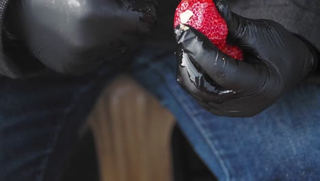 a close-up of a person's gloved hands cutting a strawberry with a knife.