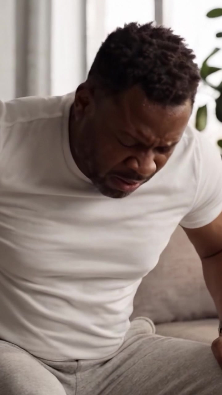 A Man Experiencing Discomfort While Sitting on a Couch: Expressions of Pain and Strain Combined with a Thoughtful Reflection in a Cozy Atmosphere