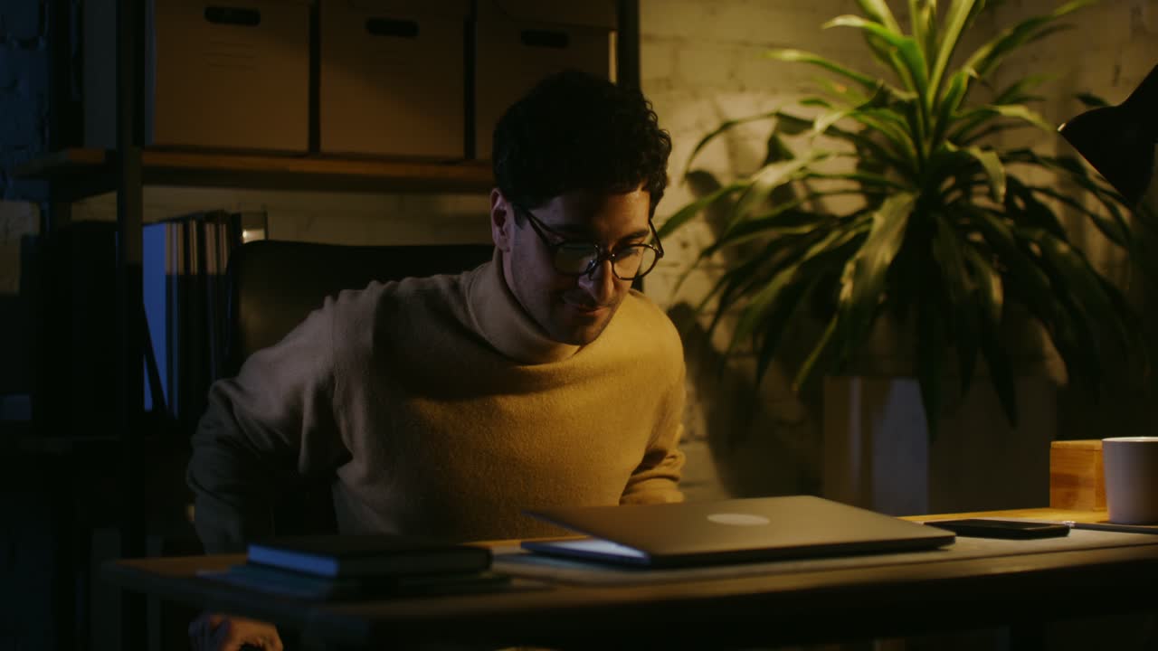 Man working late at night on laptop in a home office.