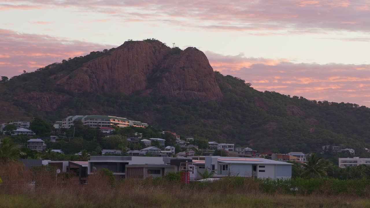 Castle Hill in Townsville at sunrise with pink and purple clouds in the sky and glowing houses at the base