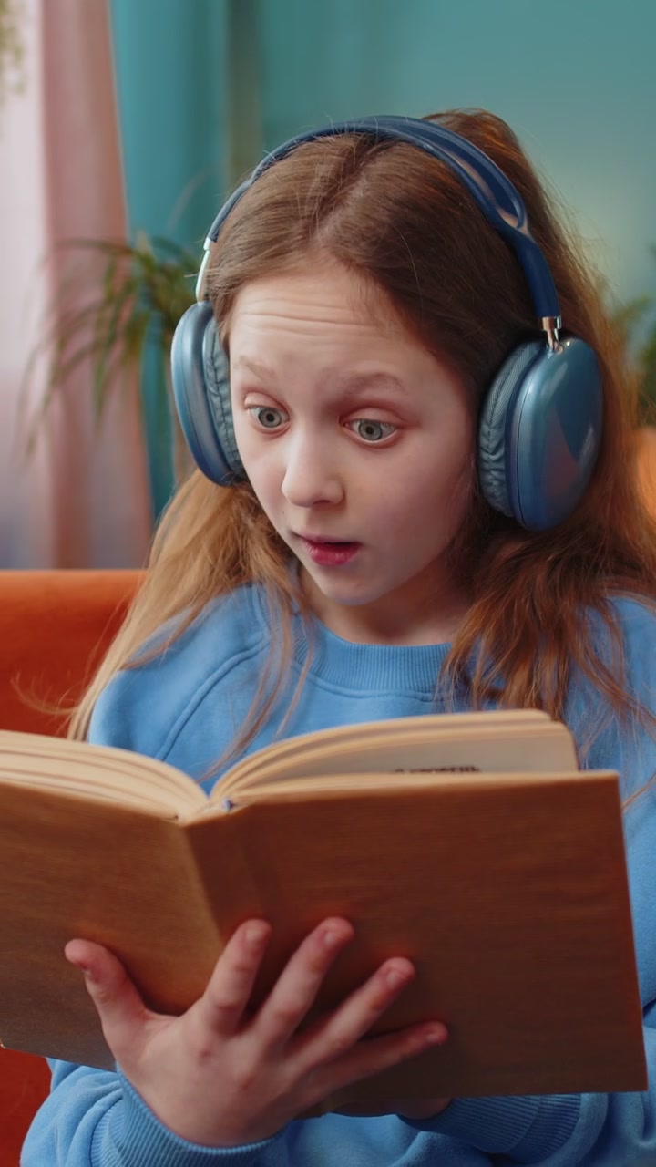 Ragazza preadolescente felice con le cuffie che legge un libro, sfoglia le pagine, sorride e si gode l'istruzione letteraria.