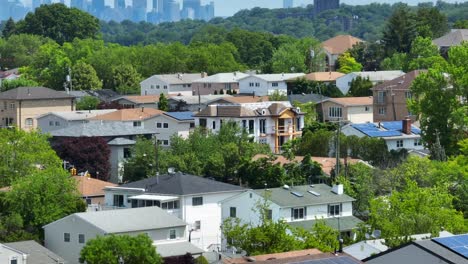 Aerial-rising-shot-of-modern-residential-area-with-solar-panels-on-roof-and-greenbelt-park-in-front-Manhattan-Skyline-Silhouette-in-background