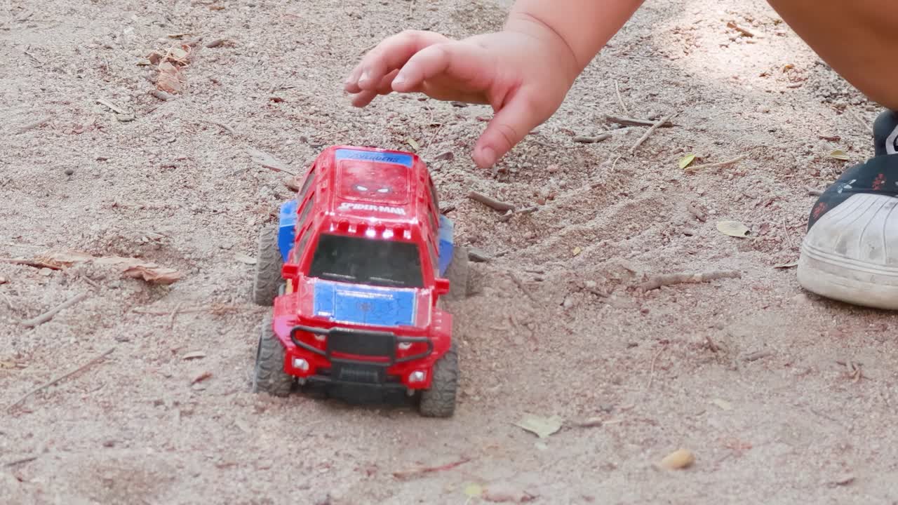 A child pushes a red toy car on sandy terrain, capturing playful interaction and movement in natural light