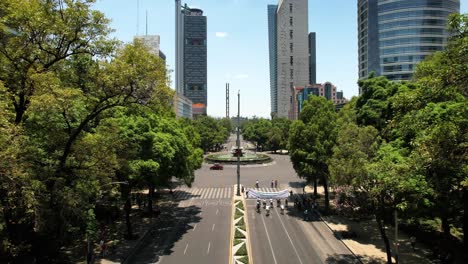 backwards drone shot of cyclists exercising on reforma avenue in mexico city during sunny day