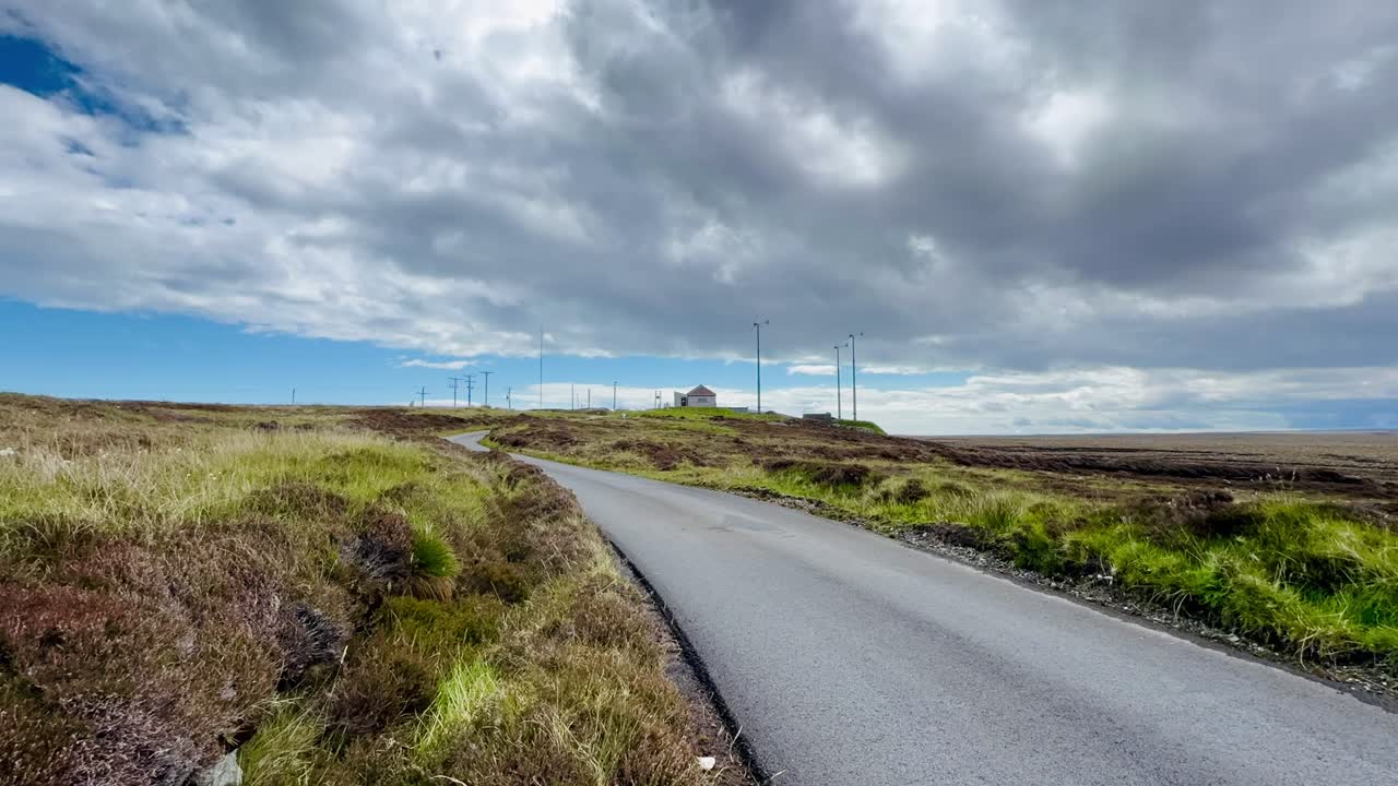 En tom landevej i Ness under en skyet sommerhimmel, der fanger hverdagen, isolationen og roen på Ydre Hebriderne i Skotland