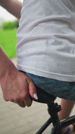 un primer plano de la mano de una mujer sosteniendo el asiento de una bicicleta mientras su hijo viaja a lo largo de una pasarela pavimentada