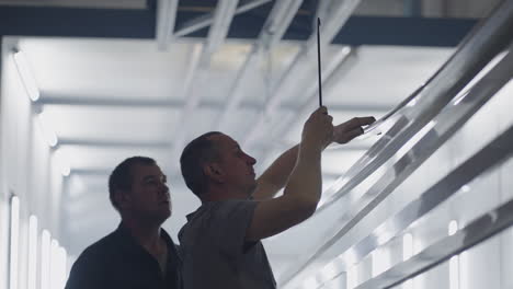 two working male painters prepare steel metal elements for painting by fixing them on suspensions. paint parts in the production room. slow-motion filming.