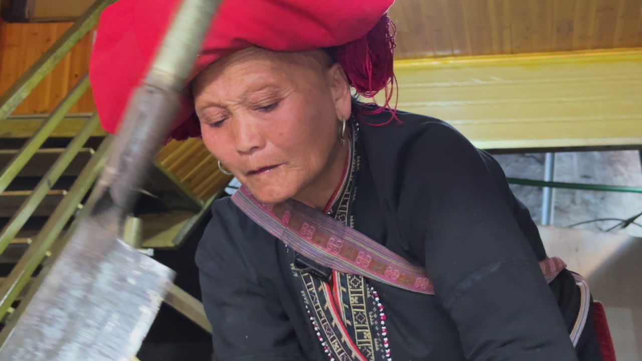 Elderly Black Dao woman forages herbs indoors, wearing traditional red headdress