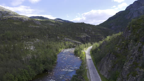 white car driving a scenic road next to a river and mountains with blue sky in the background