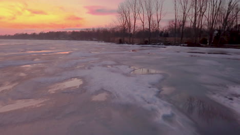 Vibrant-pink-and-orange-sunset-over-a-frozen-coastline-lake-in-southern-Ontario,-Canada