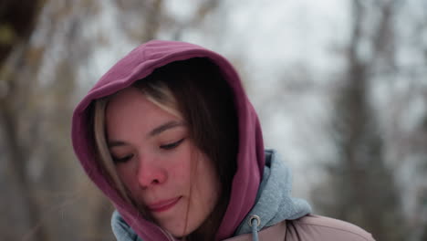 close-up of tired woman jumping in cold winter air, wearing a hooded jacket, her face shows exhaustion and determination with slightly flushed cheeks against a blurred snowy background