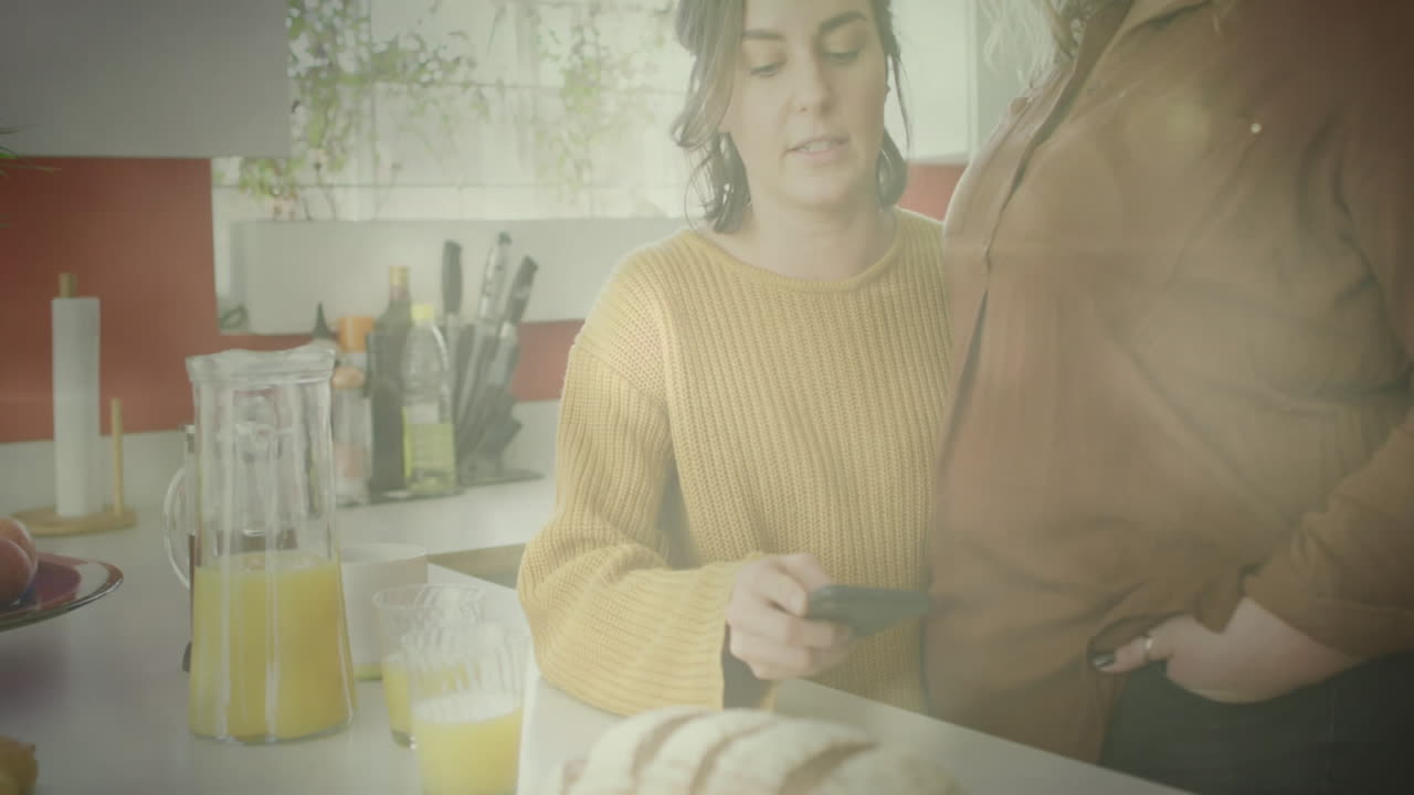 Using smartphone, person in kitchen with juice and bread, other watching animation