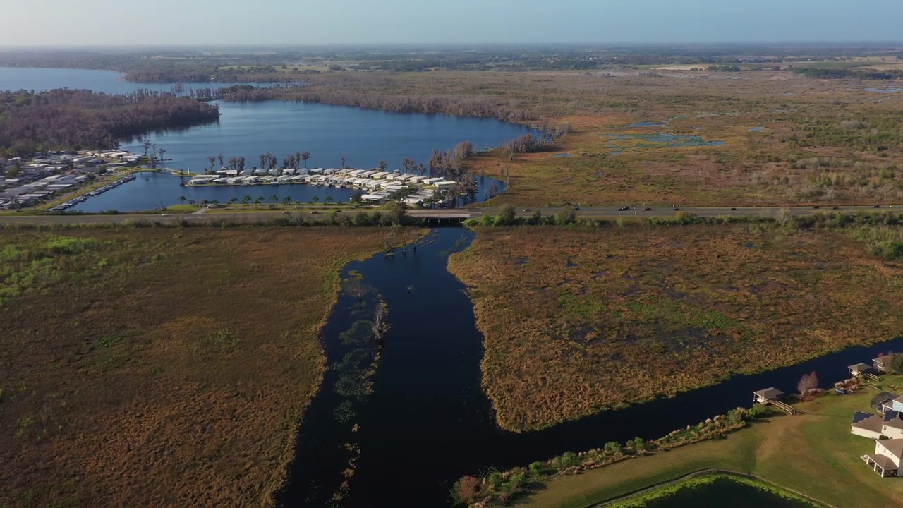 Droneoptagelse af Palatlakaha-floden, der snor sig gennem vådområder ved siden af et boligområde i Clermont, Florida, med Lake Minneola synlig i det fjerne