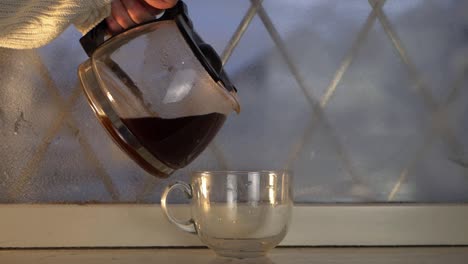 Hand-pouring-freshly-brewed-hot-coffee-in-winter-window-medium-shot