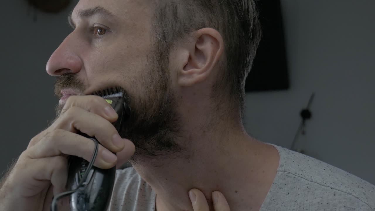 un hombre está recortando su cabello facial con una maquinilla de afeitar eléctrica para parecer atractivo