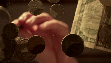 a collection of vintage coins and banknotes seen through a glass surface, with a hand reaching for them