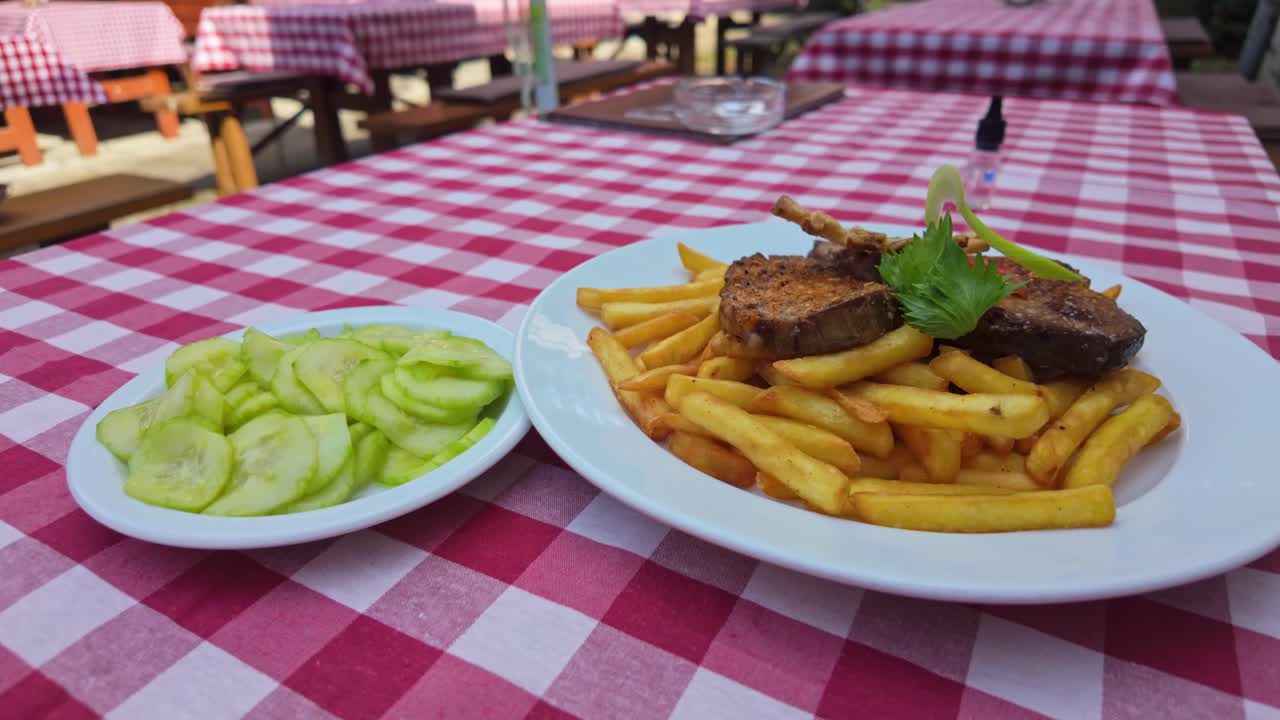 Close-up of gypsy steak with cucumber salad on a checkered tablecloth on the terrace of a traditional Hungarian restaurant