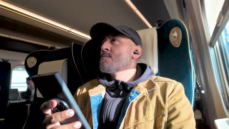 man browsing phone while traveling by train in a bright, modern interior.