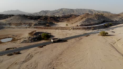 camión de carga con remolque conduciendo a través de una carretera desierta vacía temprano en la mañana en fujairah, emiratos árabes unidos rodeados de tierras áridas y montañas