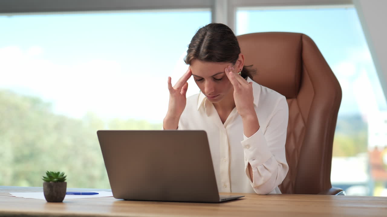 una mujer joven sufre de fuertes dolores de cabeza y agotamiento en la pantalla de la computadora portátil mientras trabaja en la oficina de casa