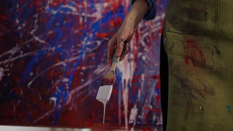 woman holding brush full of white paint then splashing it on canvas