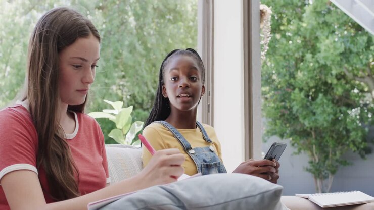Happy diverse teenage female friends sitting on couch and using smartphones in slow motion