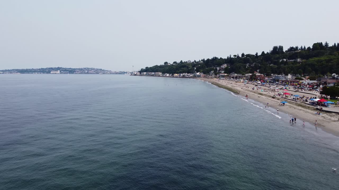 toma de drones que contrasta las tranquilas aguas del sonido de puget y las concurridas arenas de la playa de alki en seattle