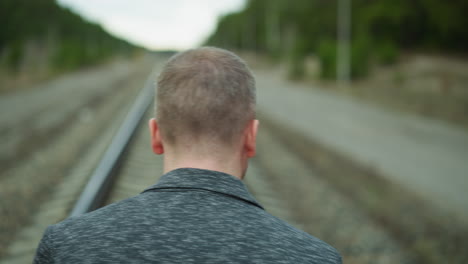 una vista de cabeza de un hombre anciano caminando solo por una vía ferroviaria, mirando a su alrededor con vista de bokeh de árboles y postes eléctricos
