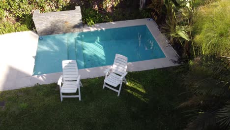 drone flying up over a garden with plastic chairs and swimming pool