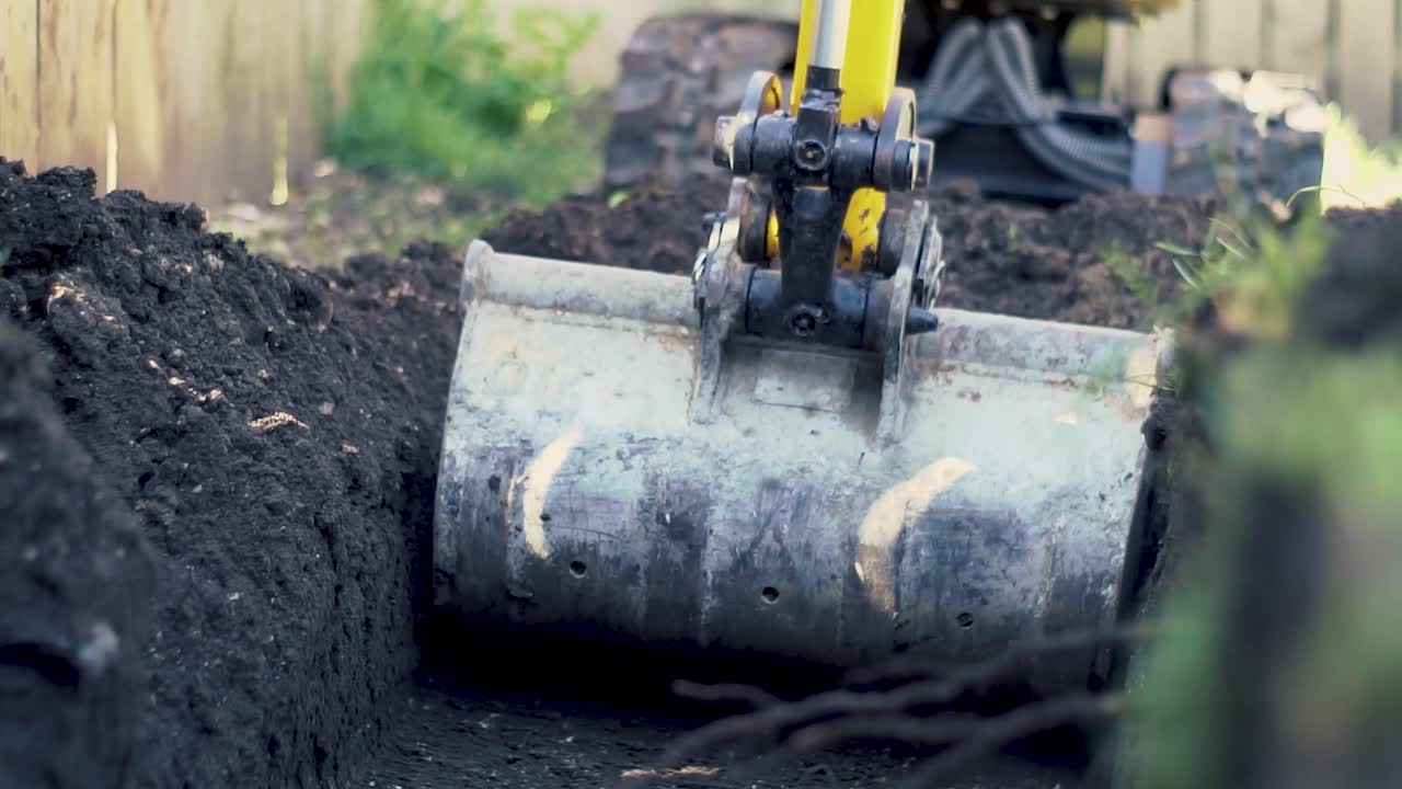 Small digger excavating soil out of a trench on a sunny day