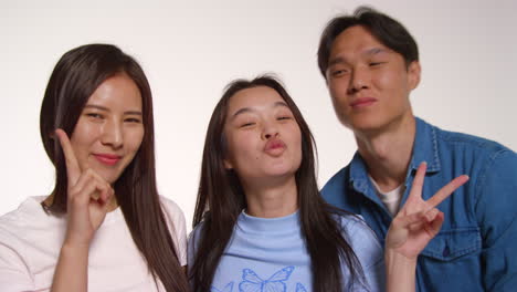 색 스튜디오 배경 앞의 젊은 친구 그룹이 사진 부스 스타일의 초상화를 위해 포즈를 취하고 있습니다.