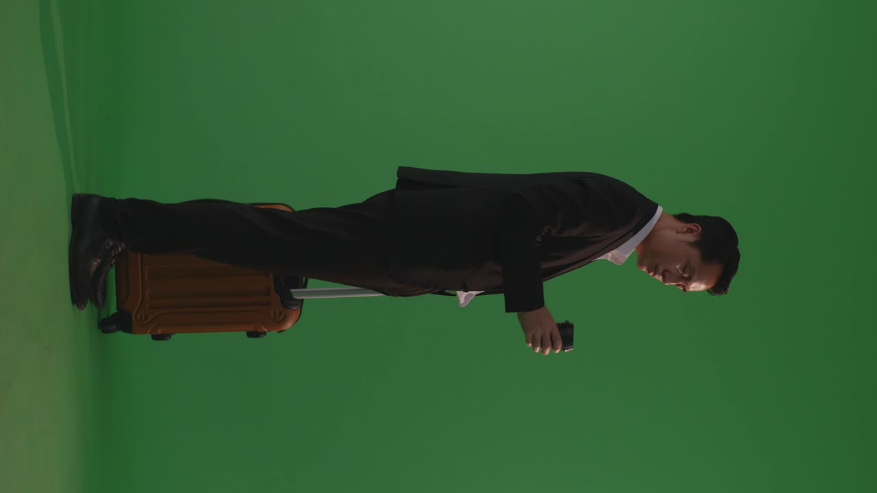 cuerpo lleno de vista trasera viajero empresario asiático con equipaje bebiendo café mientras está de pie en el estudio de fondo de pantalla verde, durante la hora de la puesta del sol