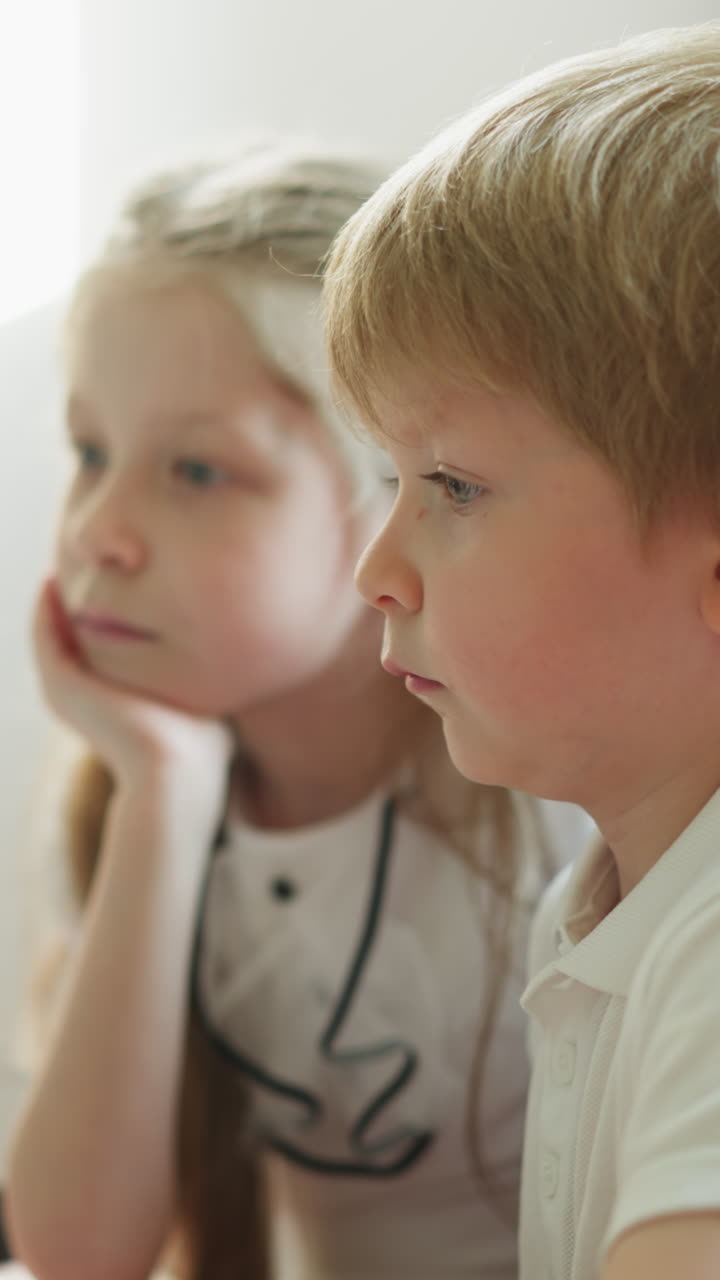 сестра и брат смотрят образовательные видео на ноутбуке в замедленном движении. мальчик и девочка сидят за столом и внимательно слушают информацию сбоку. современные технологии в школе вблизи