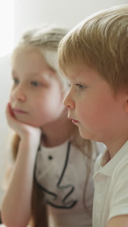 sister and brother watch educational videos on laptop slow motion. boy and girl sit at desk listening to information carefully side view. modern technologies at school closeup