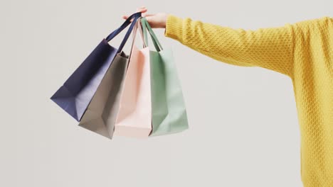 brazo de una mujer sosteniendo bolsas de regalos de colores sobre fondo blanco