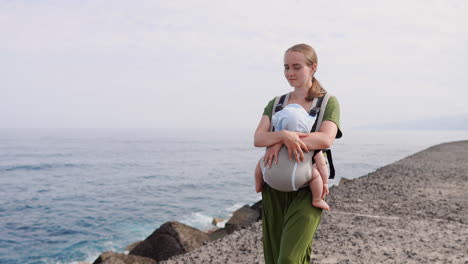 a mother and her baby share a summer day near the sea, strolling happily amidst nature. the child is safely nestled in a kangaroo backpack