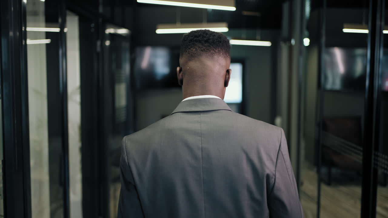 The camera follows the back of a man walking down the corridor of a business center