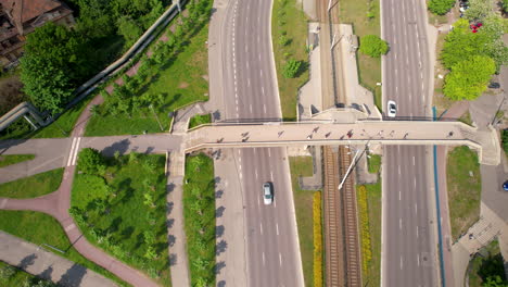 People-cross-a-bridge-over-a-multi-lane-road-in-the-city---top-down-aerial