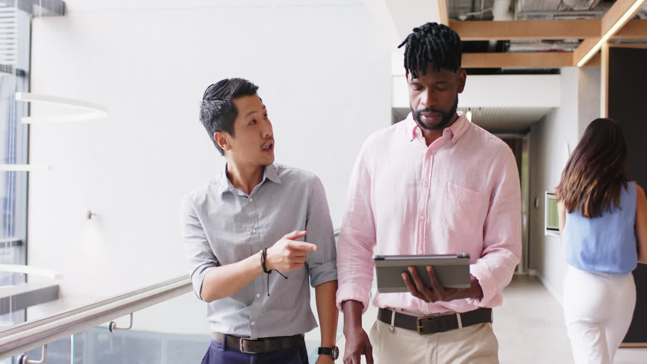 Business colleagues discussing work while walking, man holding tablet in office