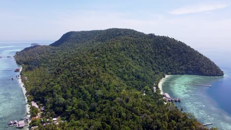 Aerial-drone-rising-over-rainforest-tree-covered-tropical-island-of-Kri-with-white-sandy-beach-coastline-and-turquoise-ocean-water-in-Raja-Ampat,-West-Papua,-Indonesia