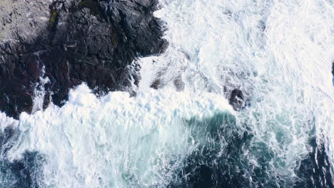 topdown aerial shot of waves building up and breaking as they hit the shore