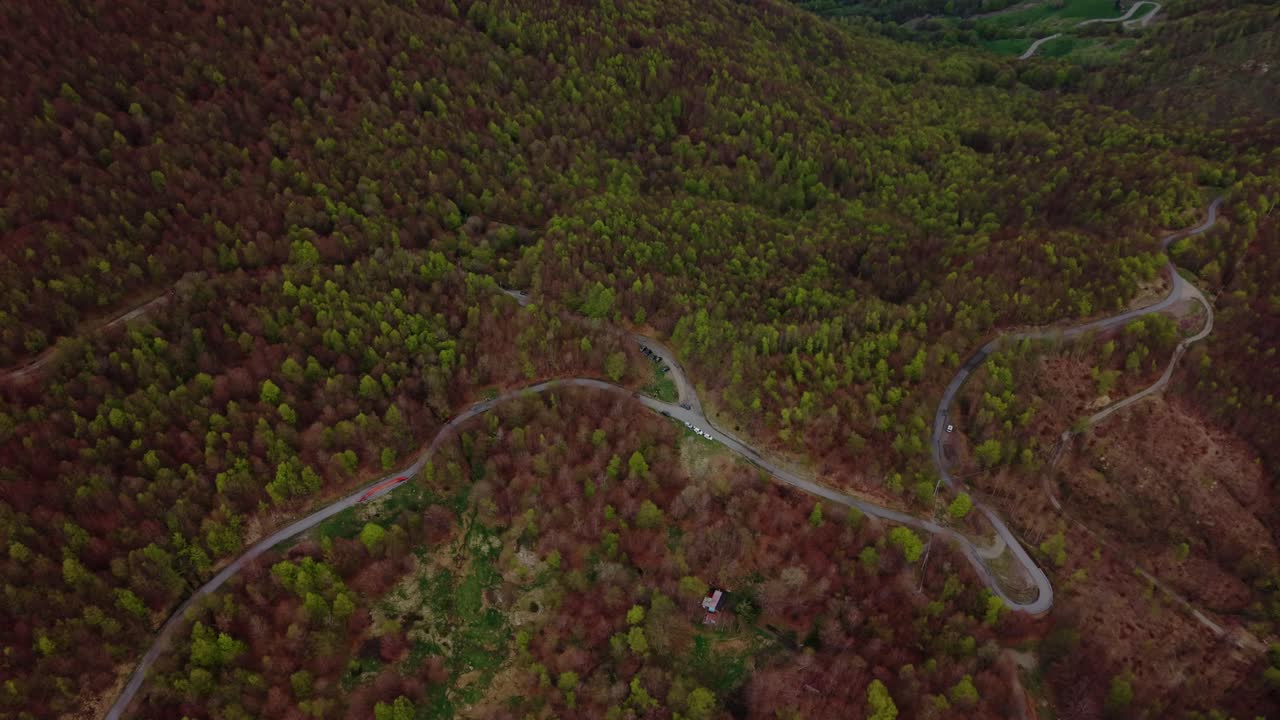 Winding mountain road leading to old radar dome, surrounded by dense forest, aerial view