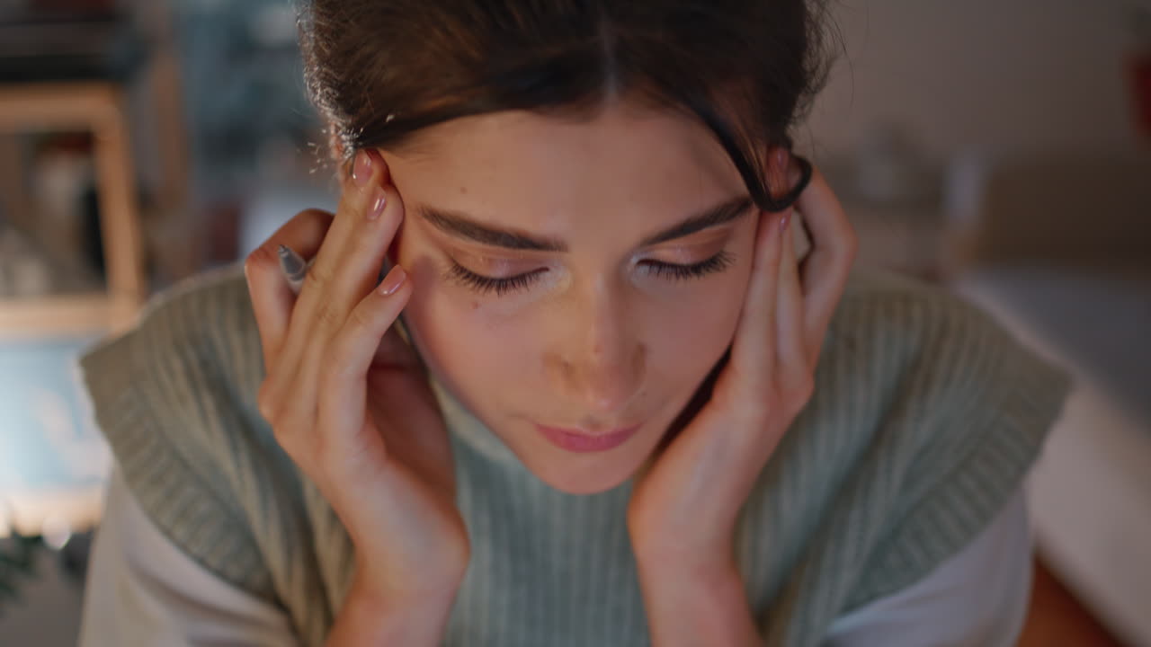 напряженная девушка массажирует голову ночью на рабочем месте вблизи. уставший студент работает