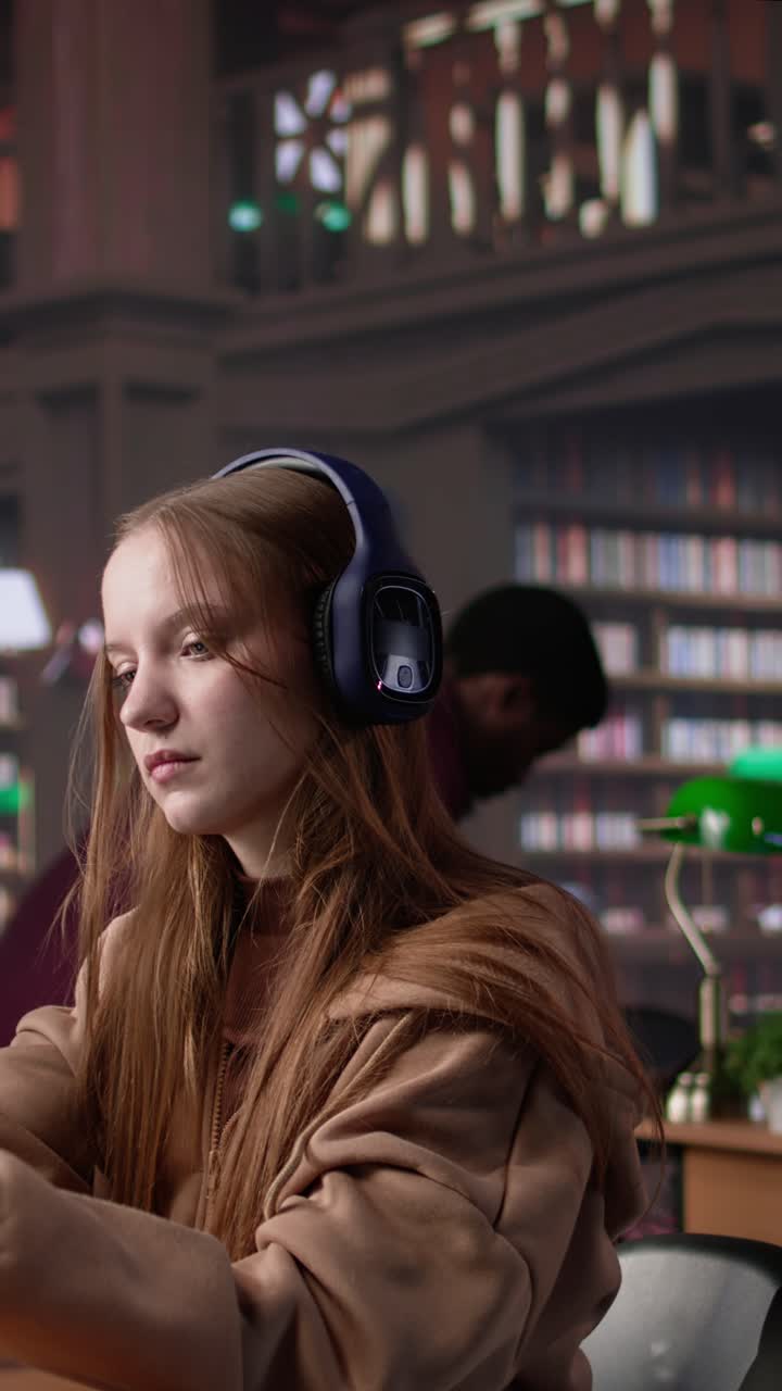 Vertical video young girl listening to educational documentary on laptop and taking notes