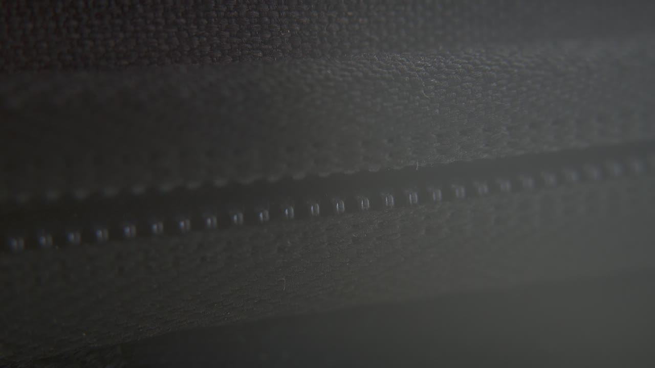A macro close-up shot of a hard case zipper being closed, metal zip, black box, photography gear, professional studio lighting, static 4K video