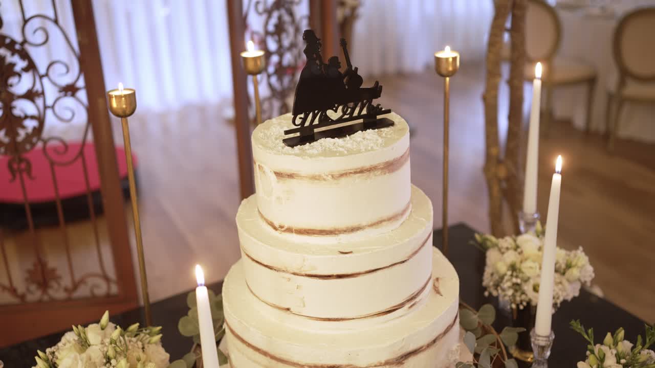 Simple wedding cake with lit candles, floral accents, and an elegant topper on display