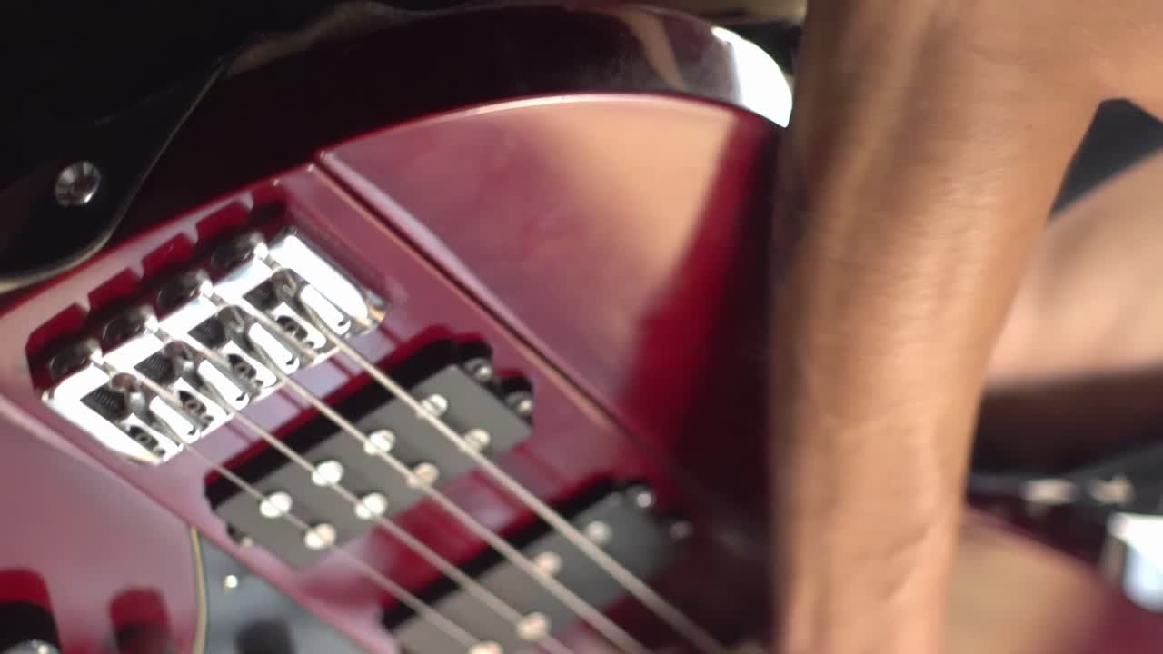Vertical close-up of male hand playing red electric bass guitar