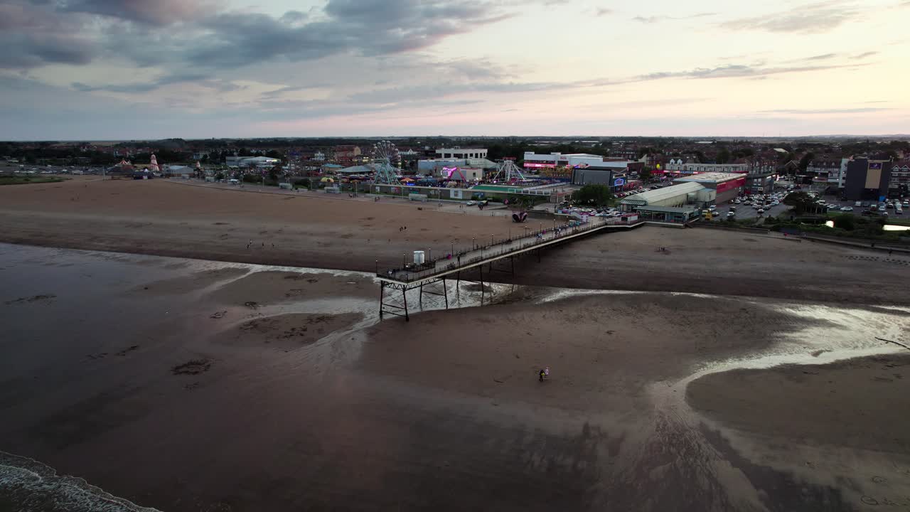 el video aéreo captura el icónico muelle de skegness durante una hermosa puesta de sol, con personas paseando a lo largo de la estructura de madera