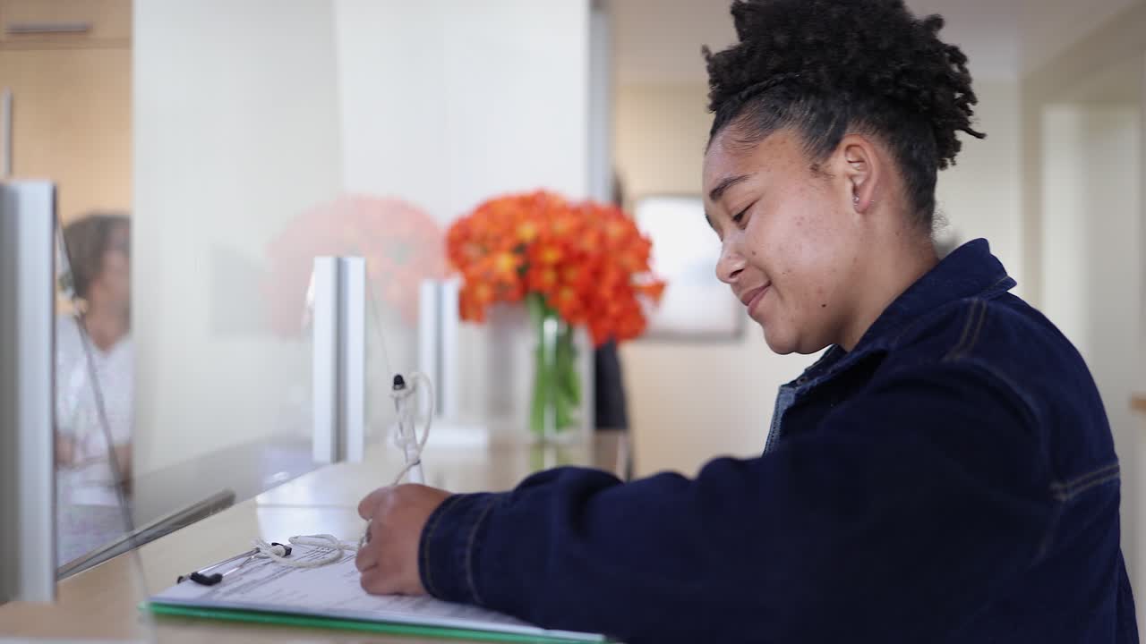 Young black woman fills out form at dental office reception counter